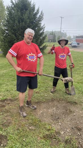 two men posing for picture while digging a hole