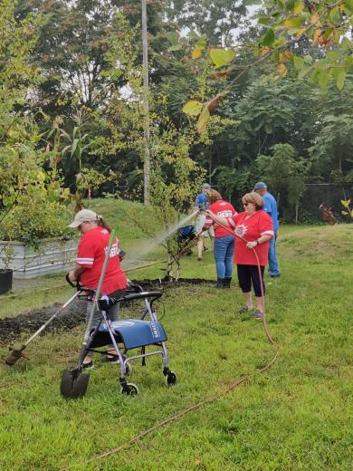 lady watering garden bed with others working around her